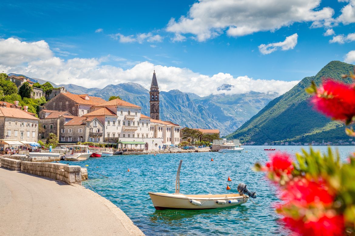 Vue panoramique pittoresque de la ville historique de Perast, dans la célèbre baie de Kotor, avec des fleurs épanouies par une belle journée ensoleillée sous un ciel bleu parsemé de nuages, au Monténégro, en Europe du Sud.