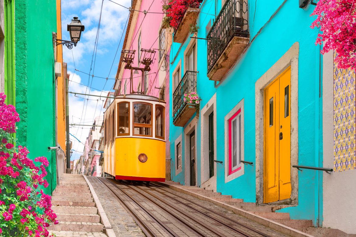 Tramway électrique jaune dans une rue bordée de maisons colorées et de fleurs aux balcons - Ascenseur Bica descendant la colline du Chiado à Lisbonne, Portugal.