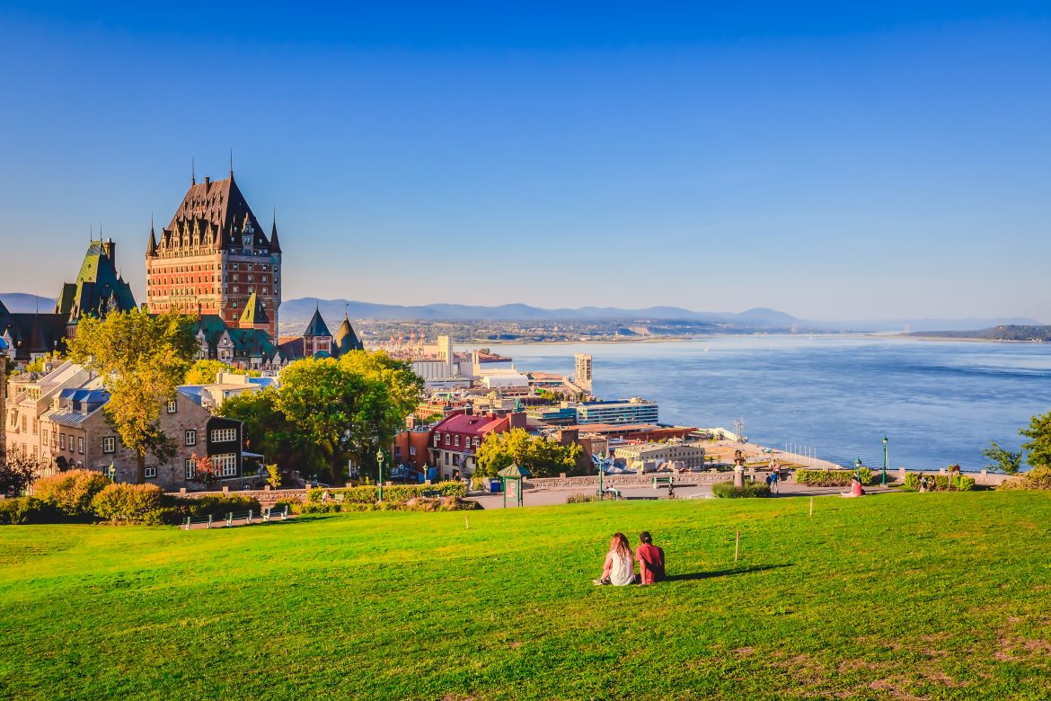 Vue panoramique du Vieux-Québec avec ses bâtiments, ses pelouses verdoyantes bordant le fleuve Saint-Laurent et le ciel bleu.