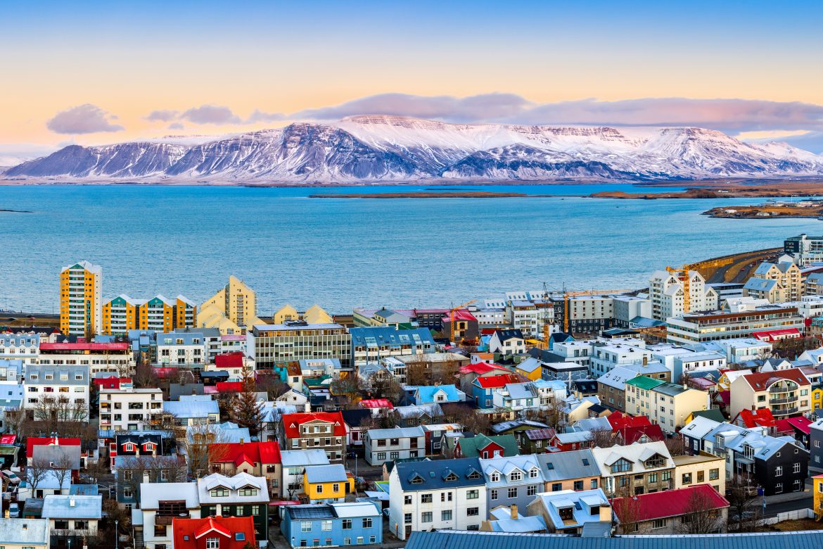 Panorama aérien du centre-ville de Reykjavik au coucher du soleil, avec ses maisons colorées et ses montagnes enneigées en arrière-plan.