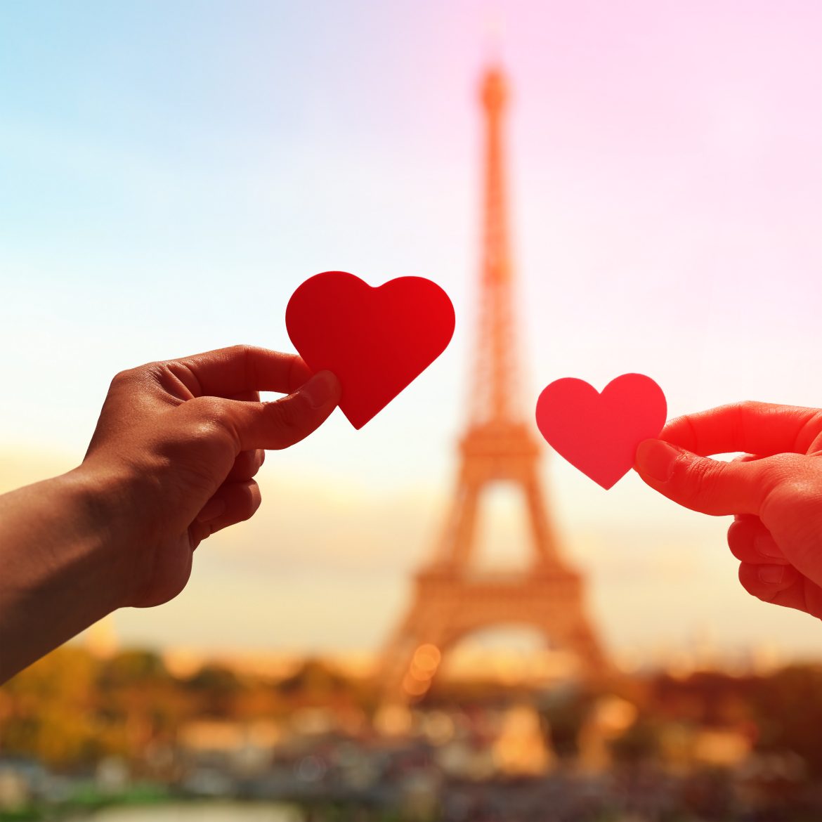 Silhouette de mains d'amoureux tenant un cœur en papier, avec la tour Eiffel à Paris au coucher du soleil.