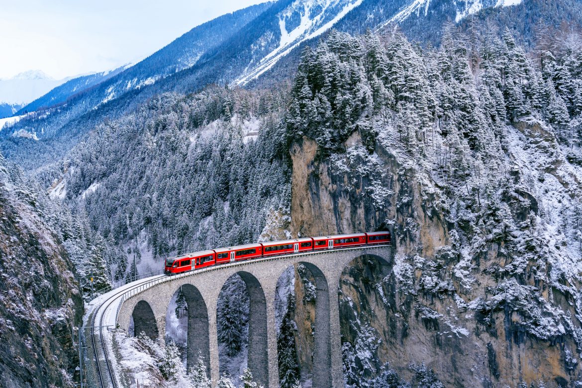 Vue aérienne d'un train traversant le célèbre viaduc de Landwasser, en Suisse. Ce viaduc, classé au patrimoine mondial, est traversé par un train express dans un paysage hivernal enneigé des Alpes suisses.
